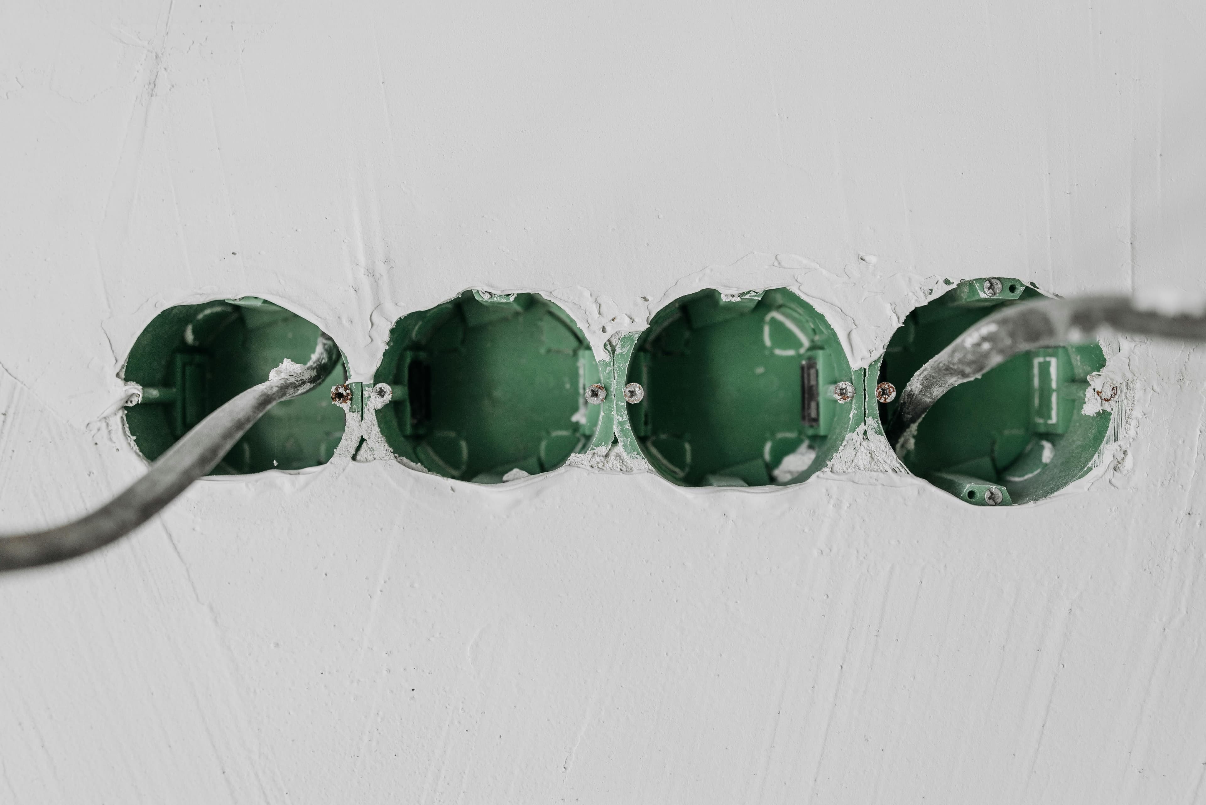 Close-up of green electrical boxes and wiring in a wall setup.