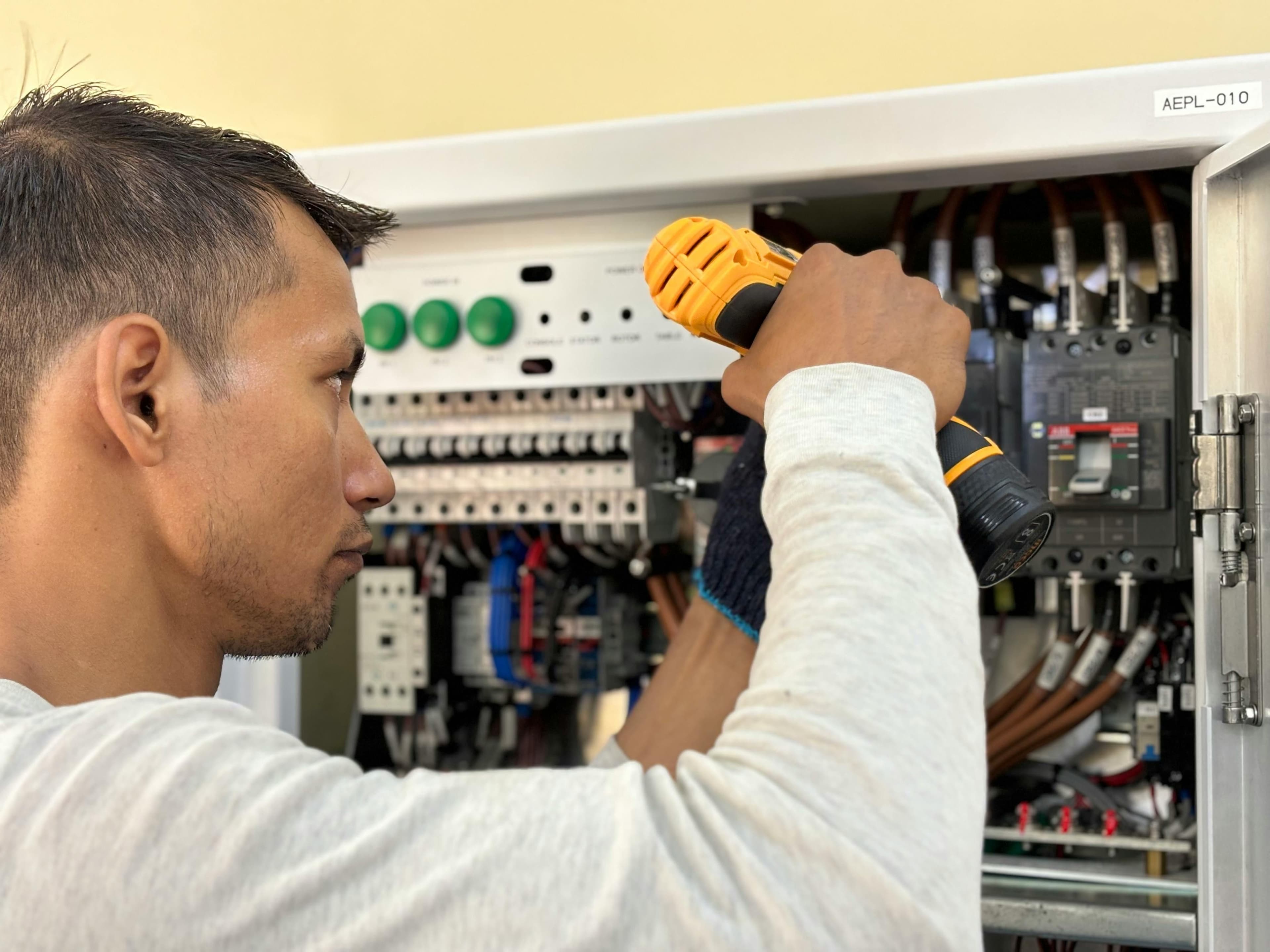 Professional electrician using a drill on an indoor circuit breaker panel.