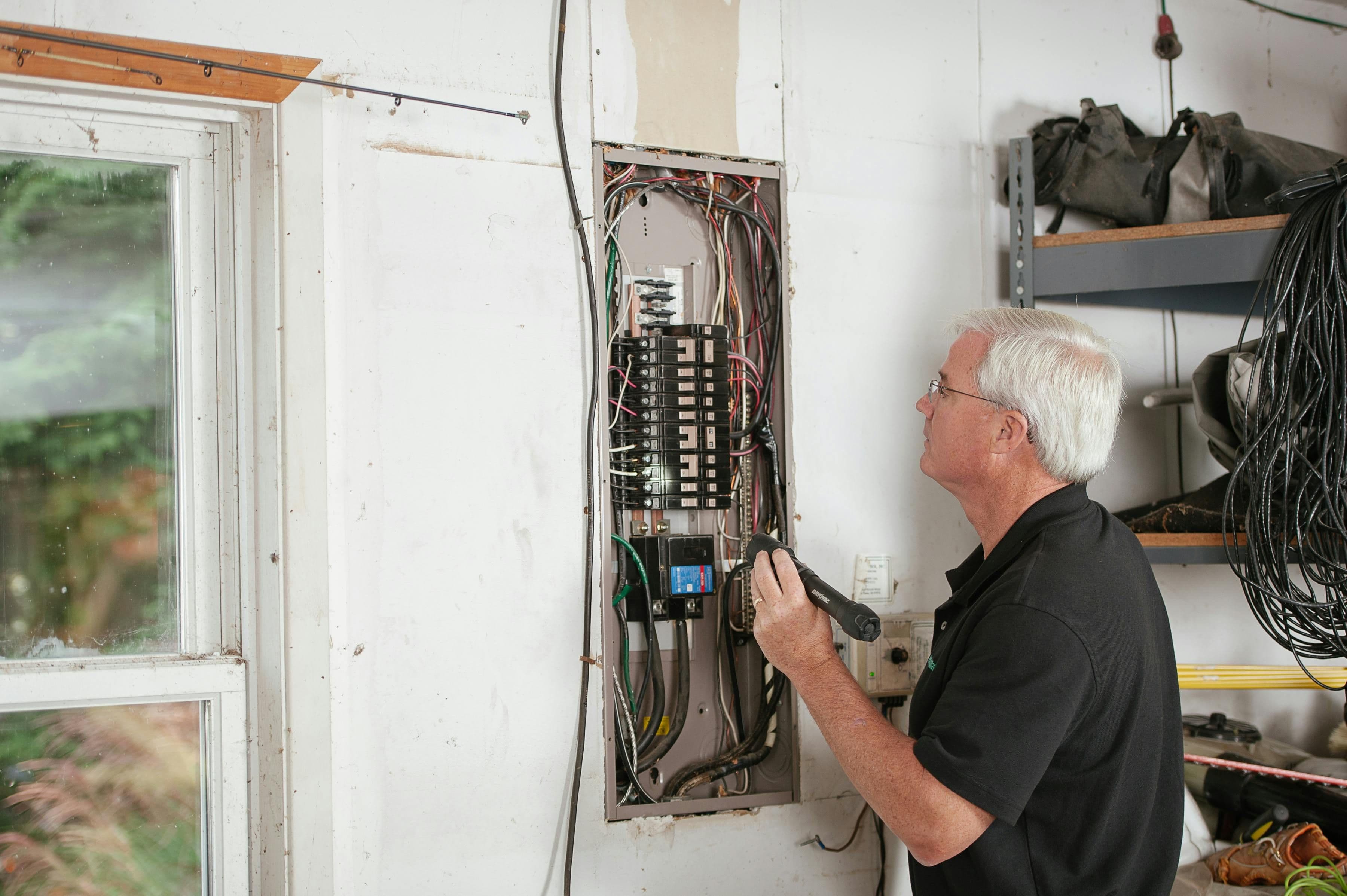 An electrician carefully examines a residential fuse box indoors, ensuring electrical safety and compliance.